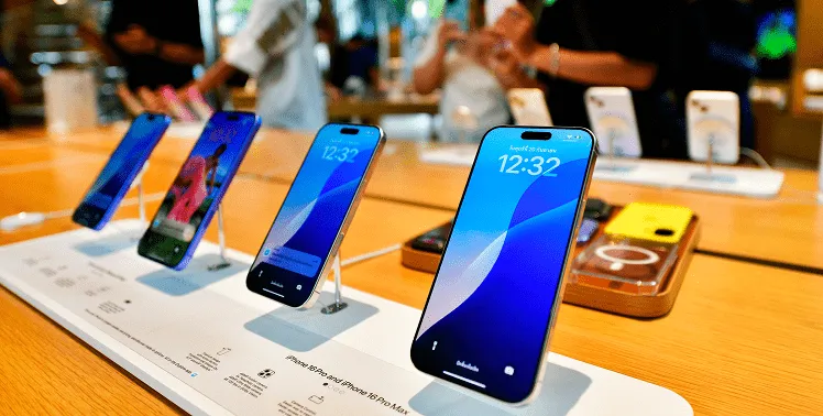 A row of iPhone 6 series devices is neatly arranged on a sleek showroom display table, each phone standing upright and showing the same lock screen time of 12:32